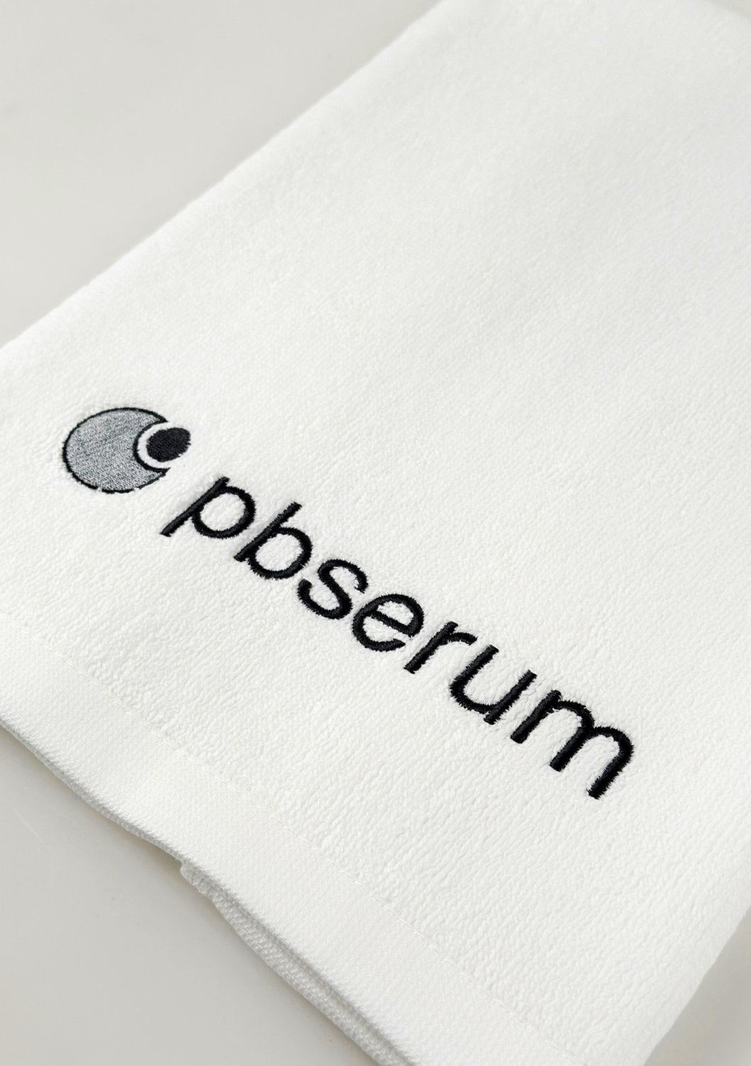 TOWEL PBSERUM SMALL, WHITE WITH GREY LOGO 
40x60 cm Malý bavlnený uterák s logom PBSerum, biely so šedou výšivkou